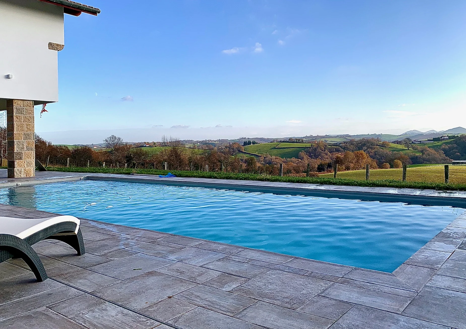 Piscine rectangulaire avec grande terrasse minérale et vue sur le paysage