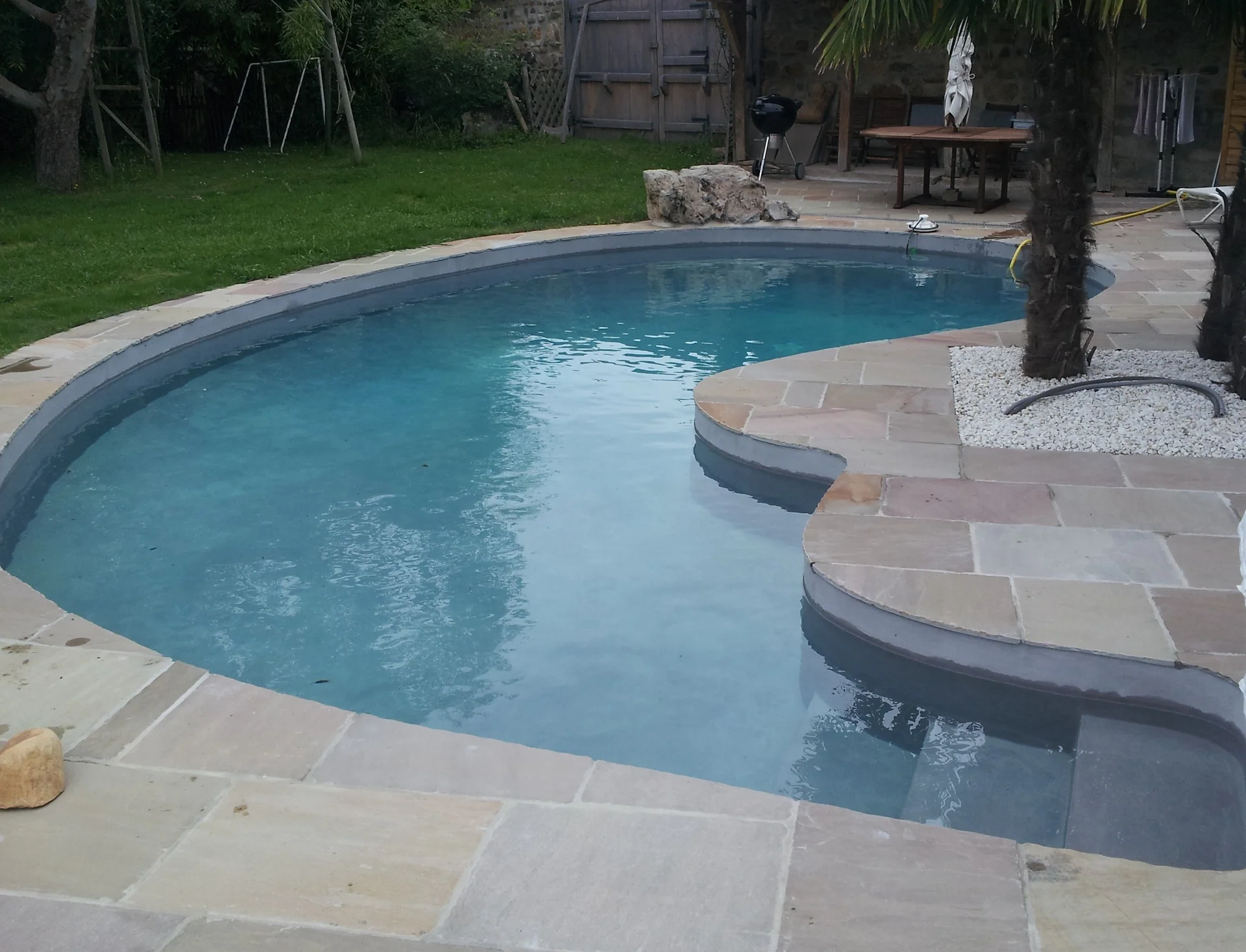 Piscine aux contours arrondis avec terrasse en pierre et escalier immergé