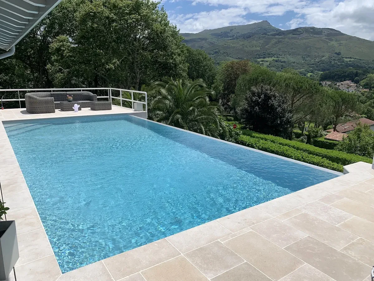 Piscine à débordement et margelles claires avec vue sur des reliefs boisés