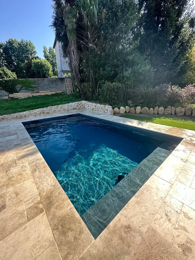 Piscine rectangulaire en eau entre terrasse minérale et jardin arboré