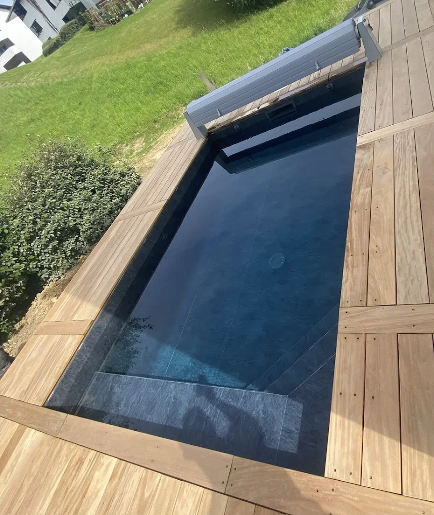 Piscine sombre entre des plages en bois avec volet enroulé en bout de bassin