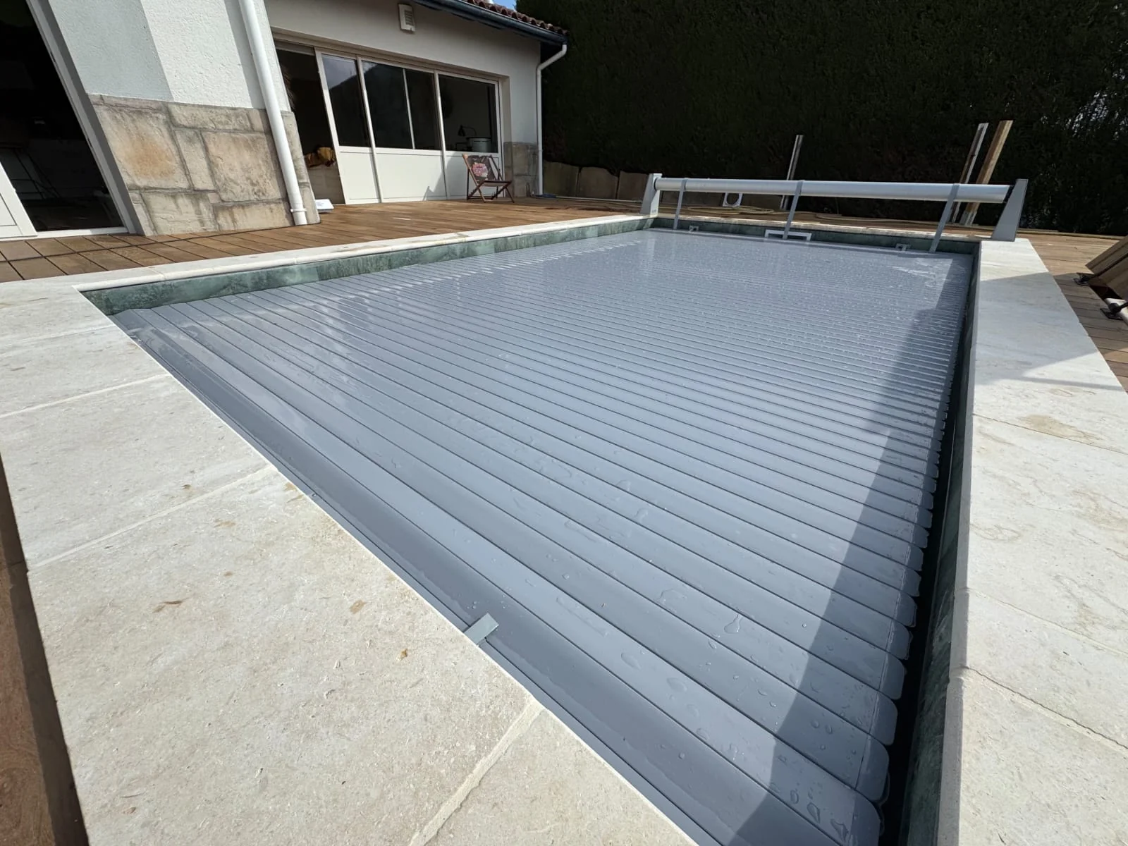 Volet roulant fermé sur une piscine bordée de pierre et de bois